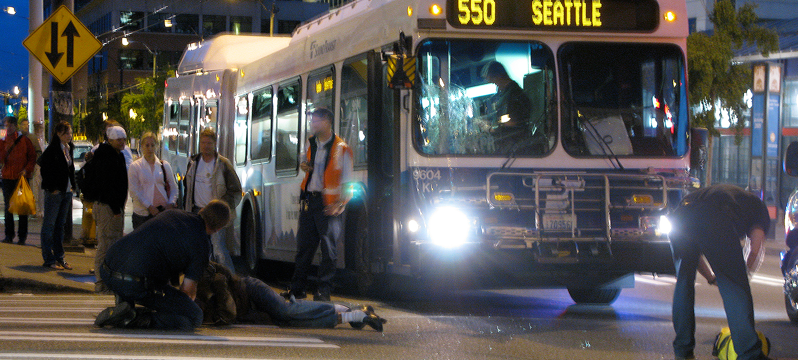 Pedestrian hit by bus lies on the ground while being assisted by law enforcement personnel.